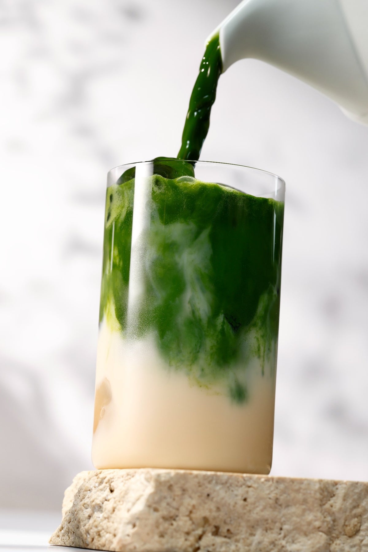 Matcha being poured into a glass of oat milk, close-up