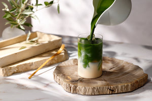 Matcha being poured into a glass of oat milk on a wooden board