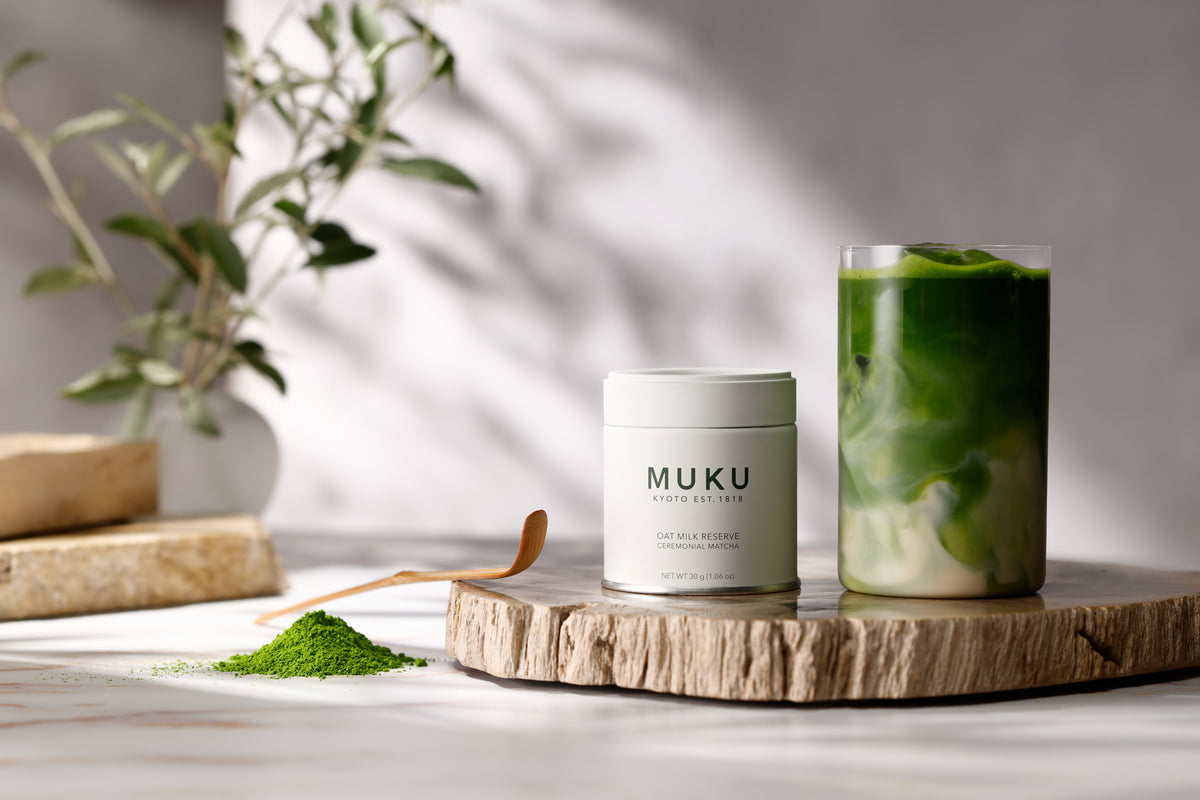 MUKU Oat Milk Reserve 30g tin beside an oat milk matcha latte on a wooden board