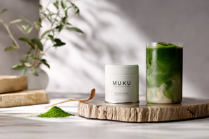 MUKU Oat Milk Reserve 30g tin beside an oat milk matcha latte on a wooden board